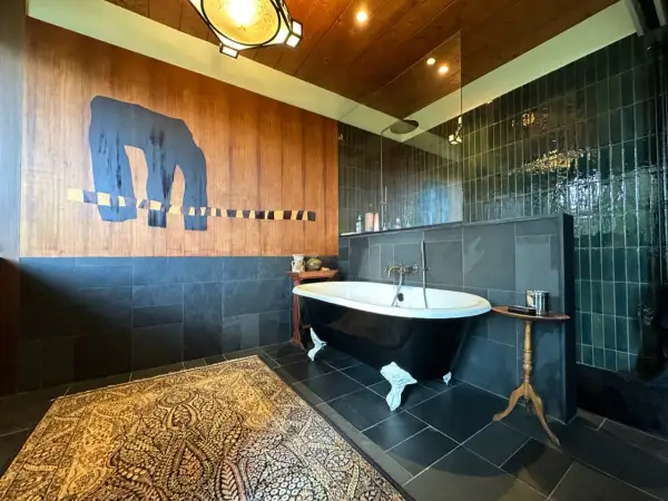 Salle de bain moderne avec baignoire sur pieds noire, tapis persan et mur boisé orné d'une œuvre d'art abstraite. Une **rénovation baignoire** réussie.