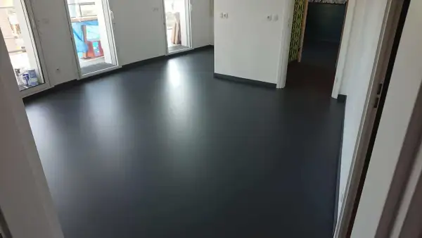 Un sol en résine époxy noir brillant, fraîchement posé, reflète la lumière dans un intérieur moderne.