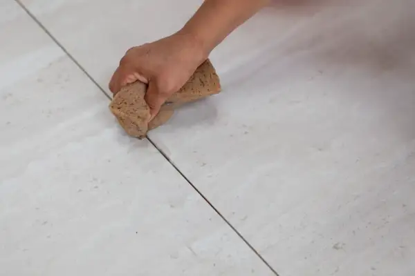 Main d'une personne nettoyant le joint carrelage avec une éponge.