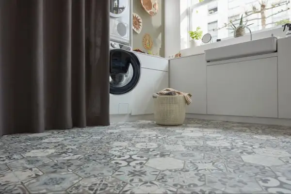 Buanderie moderne avec un sol en carrelage hexagonal aux motifs vintage. Une machine à laver et un panier à linge sont visibles.