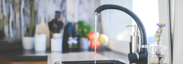 Un robinet moderne coule dans une cuisine. Un préparateur ECS discret est visible à l'arrière-plan, à côté d'un distributeur de savon.